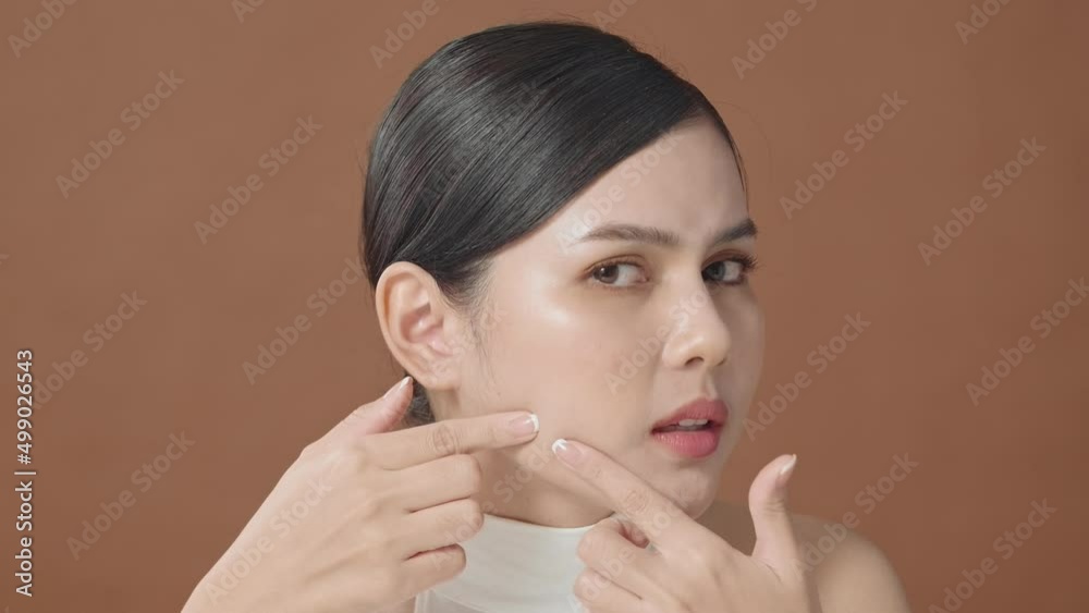 Young beautiful woman is checking her skin and popping pimple over brown background Young beautiful woman is checking her skin and popping pimple over brown background
