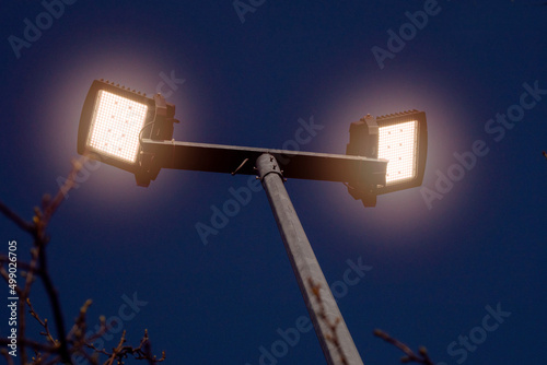 Powerful LED light on a aluminum metal pole, dark blue sky background. Concept sport event, game. Modern light source. Warm light color.