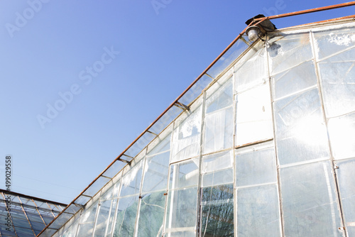 Old destroyed greenhouse with broken window glasses and rusty frame. Urban ruined geometry. Blue sky.