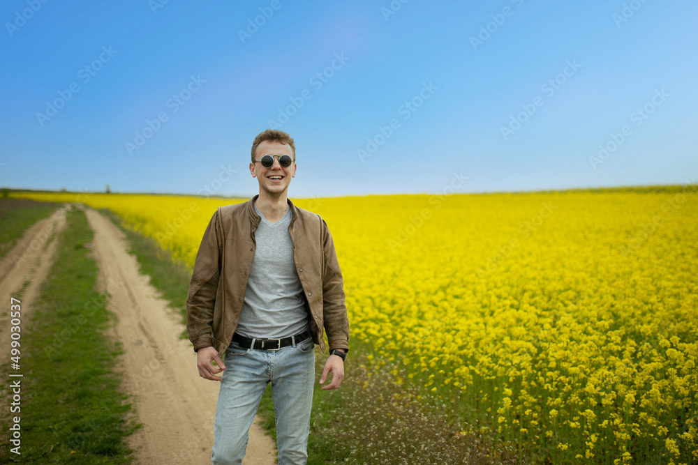 man in a leather jacket in a field against the backdrop of blooming rapeseed and a blue sky, blue and yellow colors.