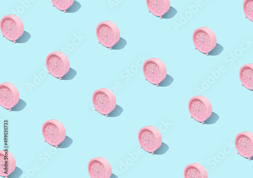 Trendy pattern made with pink clock on bright and pastel blue background. Minimal time concept. Chrismas eve or new year idea.