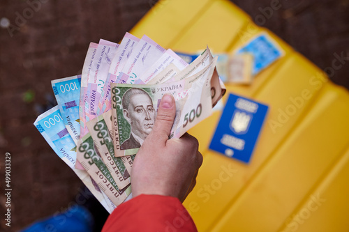 The girl holds Ukrainian hryvnia against the background of a yellow suitcase and a passport of Ukraine. Ukrainian symbols. Refugees and IDPs from Ukraine 2022. photo