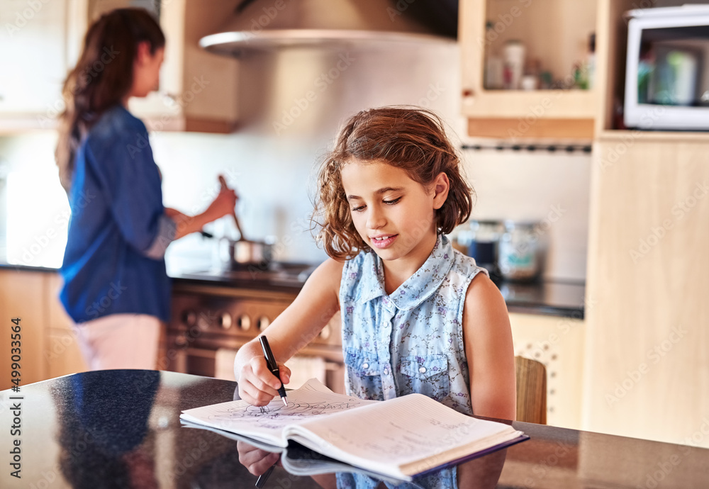 Passing the time while mom prepares lunch. Cropped shot of a young girl writing in a book while her mom cooks in the background.