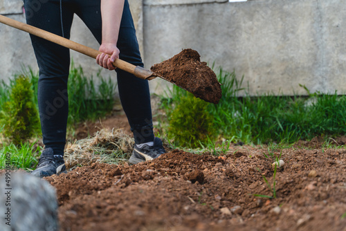 A man is digging a hole with a shovel for a plant in his backyard garden during the day