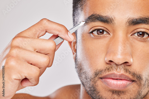 On my way to perfect eyebrows. Shot of a young man plucking his eyebrows against a grey background.
