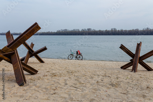 Abandoned bicycle on empty river bank with czech anti-tank hedgehoges. Interrupted life in Ukrainian cities. Russian invasion, war in Ukraine 2022