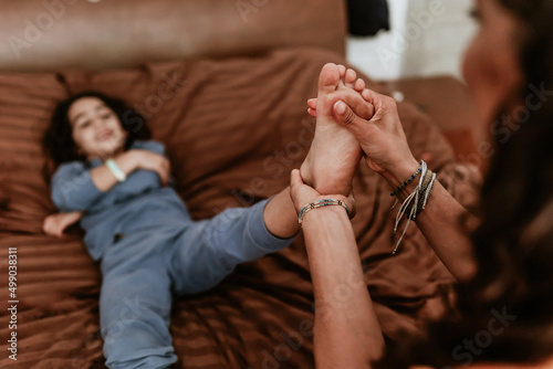 Hispanic Mother putting cream, ointment or balm to her son on the foot on bed at home in Mexico Latin America