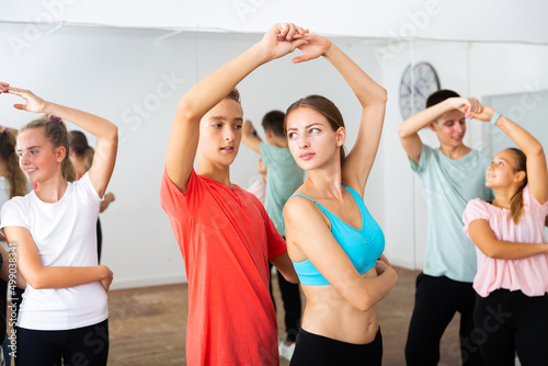 Teenagers dancing together slow ballroom dances in pairs in choreography class with young female trainer