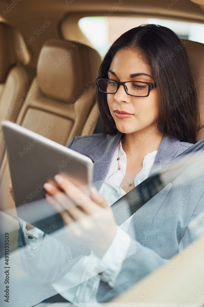 Getting a business update while on the move. Shot of a young businesswoman using her digital tablet while sitting in the backseat of a car. Getting a business update while on the move. Shot of a young businesswoman using her digital tablet while sitting in the backseat of a car.