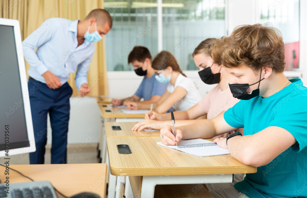 Obraz premium Portrait of teenager in protective face mask writing in workbook on lesson. New life reality during COVID pandemic