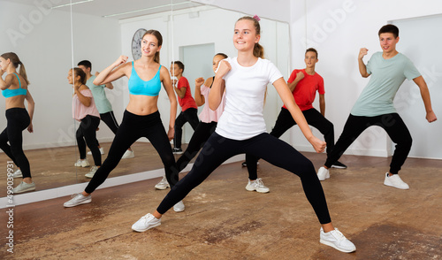 Group of teenagers participating in dance class, following their young female teacher in dance school