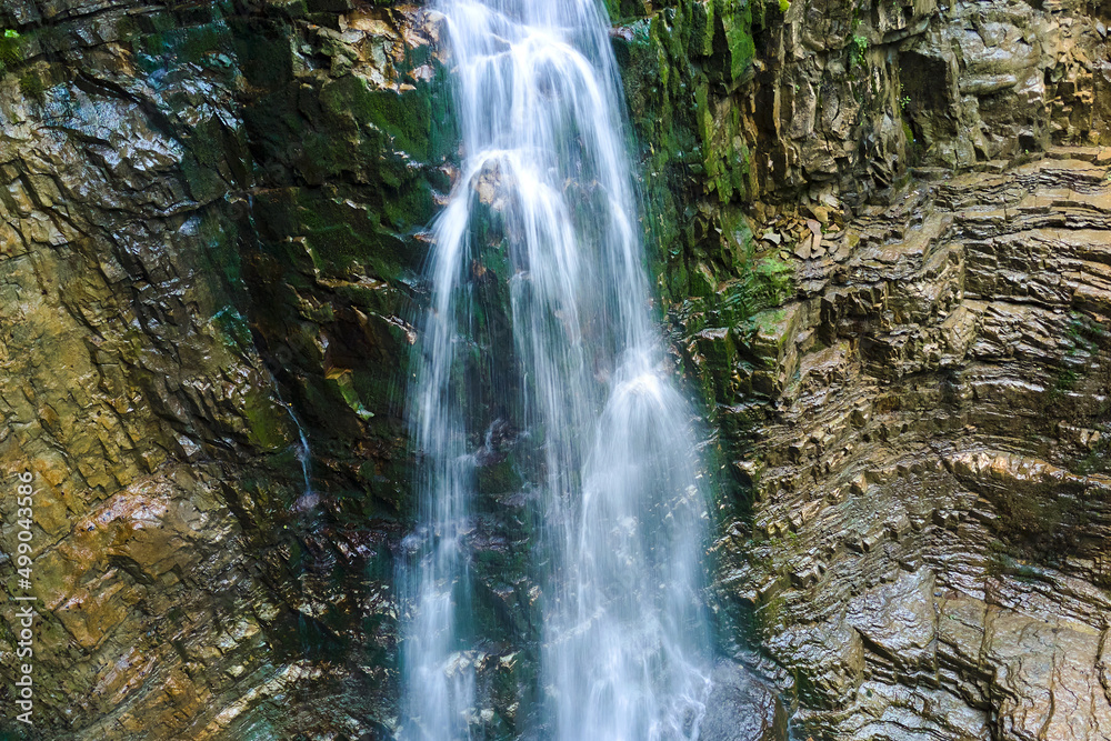 Waterfall on mountain river with white foamy water falling down from rocky formation in summer forest Waterfall on mountain river with white foamy water falling down from rocky formation in summer forest