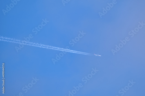 Distant passenger jet plane flying on high altitude on clear blue sky leaving white smoke trace of contrail behind. Air transportation concept