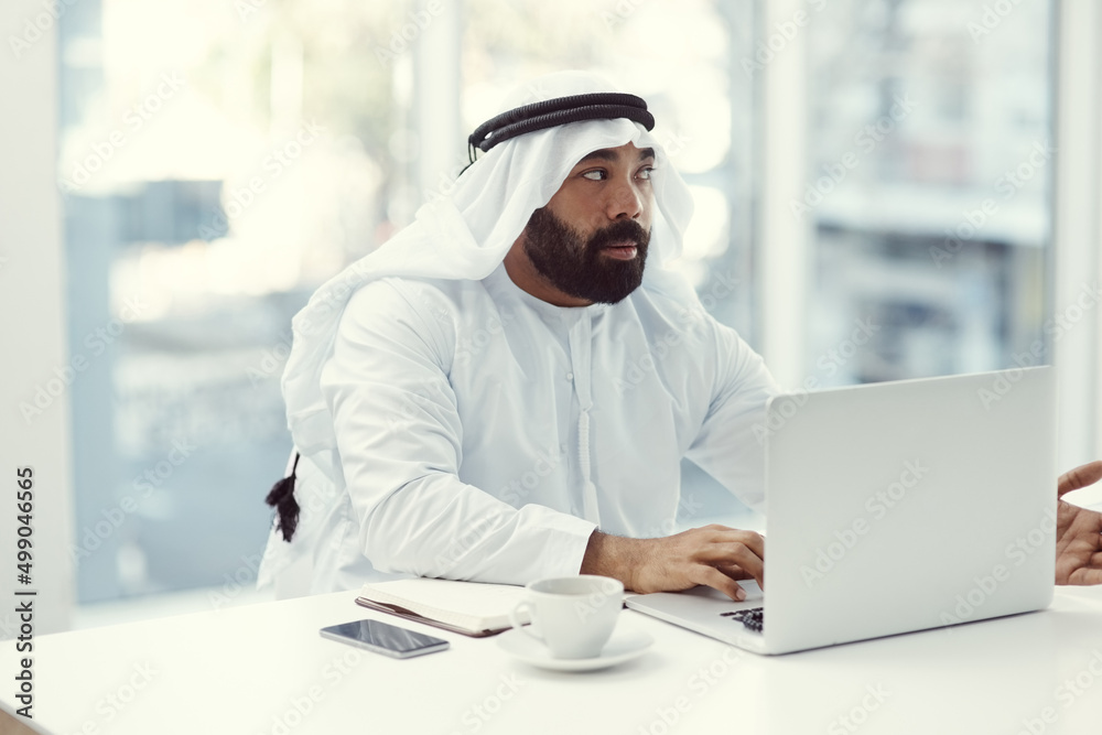 Hes got an idea. Cropped shot of a young businessman dressed in Islamic traditional clothing working on his laptop while sitting in the office. Hes got an idea. Cropped shot of a young businessman dressed in Islamic traditional clothing working on his laptop while sitting in the office.