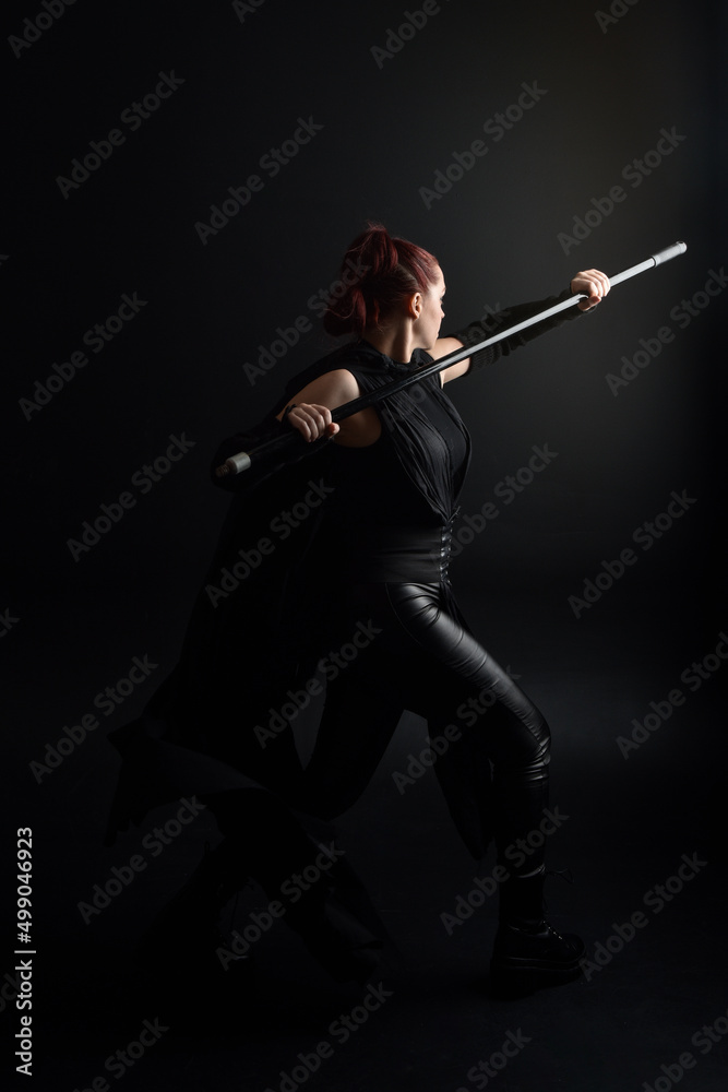 Full length portrait of pretty redhead female model wearing black futuristic scifi leather cloak costume. Standing pose on dark studio background with shadow rim moody lighting. Full length portrait of pretty redhead female model wearing black futuristic scifi leather cloak costume. Standing pose on dark studio background with shadow rim moody lighting.