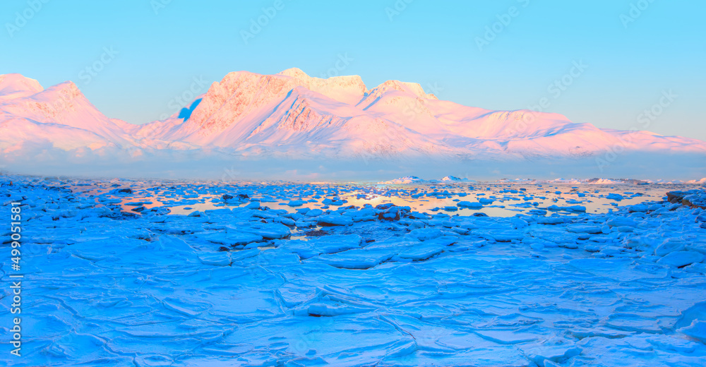 Panoramic view at fjord with coast of the Norwegian Sea in the background snowy mountains Arctic Circle at sunset - As a result of melting snow, freezing of the water mixed with the sea - Norway