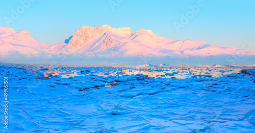 Fototapeta Naklejka Na Ścianę i Meble -  Panoramic view at fjord with coast of the Norwegian Sea in the background snowy mountains Arctic Circle at sunset - As a result of melting snow, freezing of the water mixed with the sea - Norway