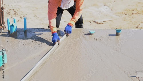Worker plastering smooth floor surface with screeder. Floor cement work.  photo