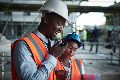 Quality construction inspired by teamwork. Shot of a young man using a walkie talkie while working with his colleague at a construction site.