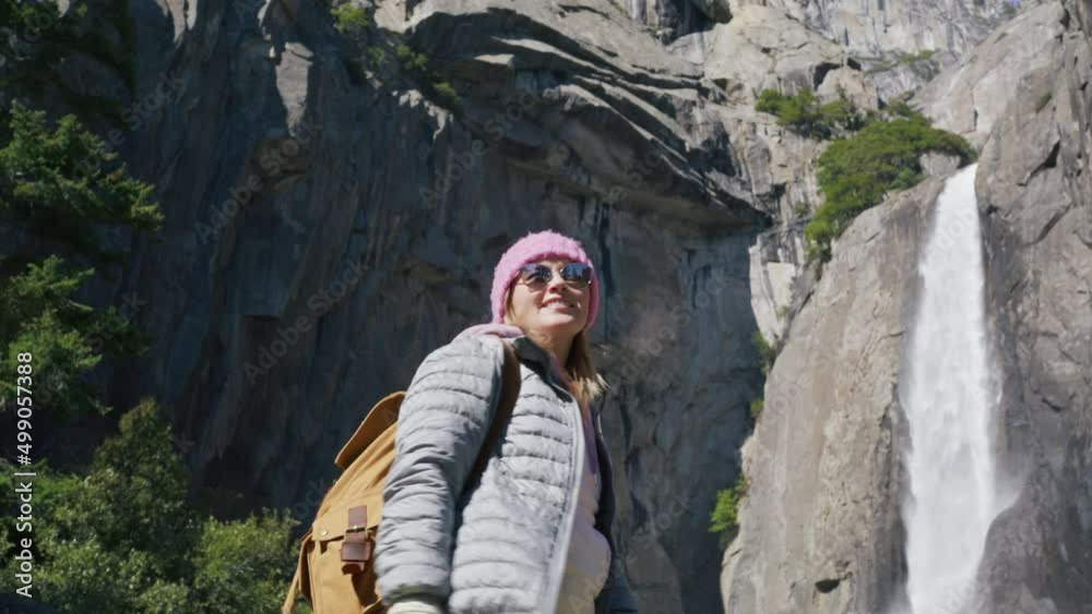 Young woman with tourist backpack looking at scenic waterfall on top of mountain Young woman with tourist backpack looking at scenic waterfall on top of mountain