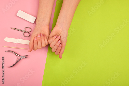 Hands with natural color manicure next to instruments for the procedure on green background © demphoto