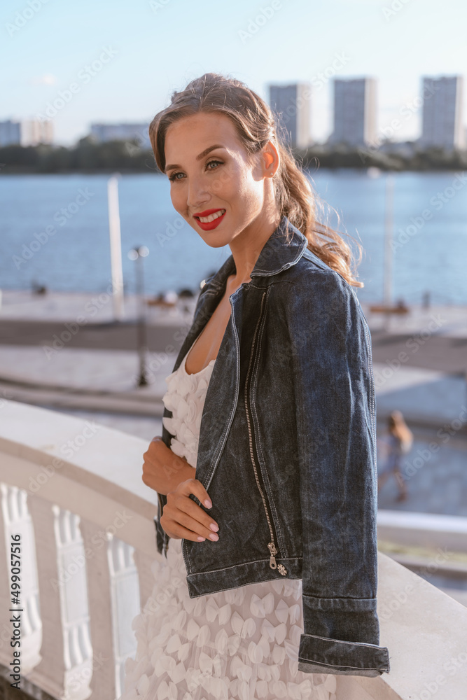 An attractive woman celebrates life in a summer white dress and denim jacket on the balcony of a summer resort. Joy and serenity An attractive woman celebrates life in a summer white dress and denim jacket on the balcony of a summer resort. Joy and serenity