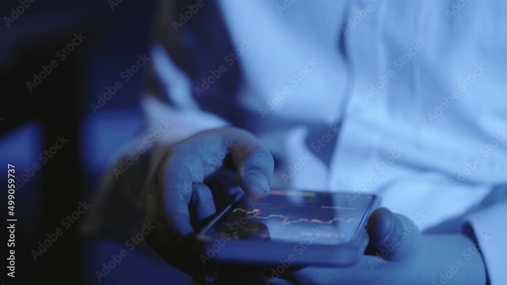 A close-up of a man's hand with a phone, the screen shows an online stock market chart showing bitcoin currencies. In blue light. In real time. Cryptocurrency. Investors