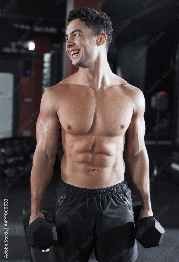 You can see the work hes put in. Cropped shot of a handsome and buff young man working out with dumbbells while shirtless in the gym.