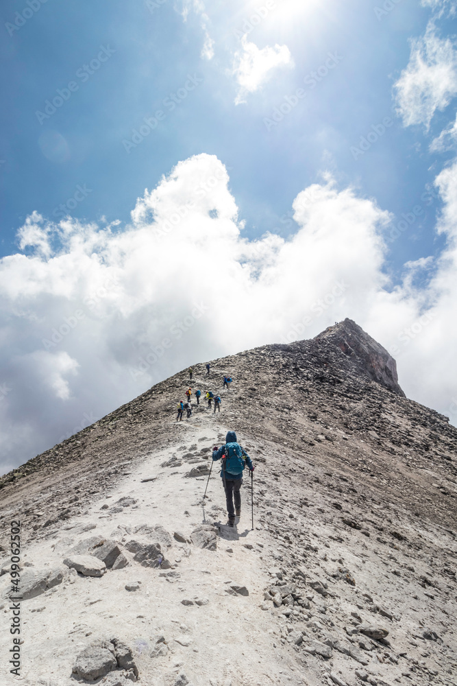 woman with backpack walking towards a group of hikers reaching the top of a mountain