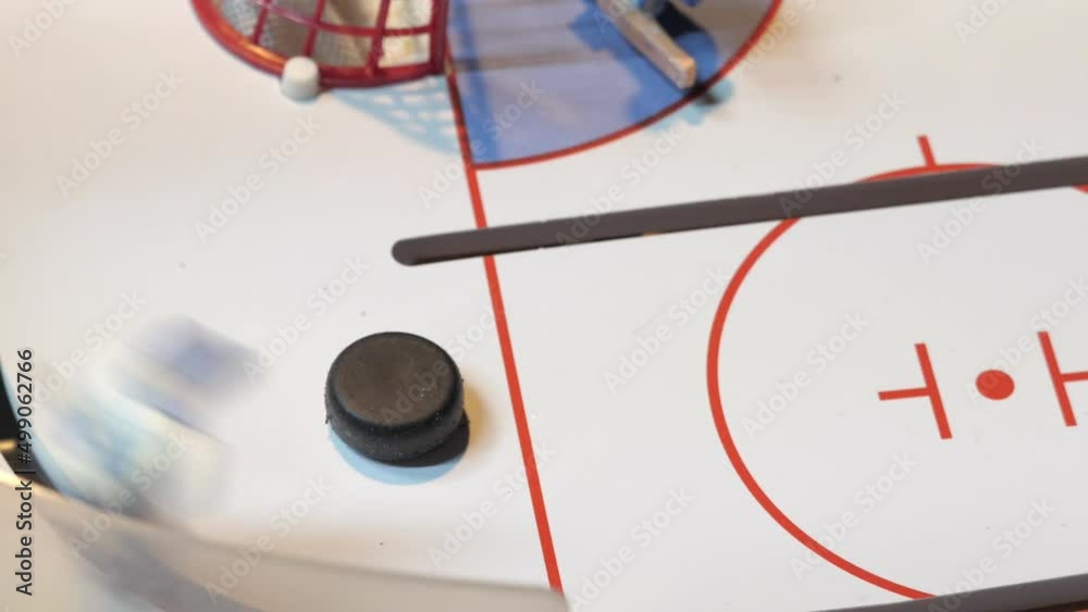 Attack of miniature hockey player figures kicking puck on toy ice rink of board game in light room extreme close view Attack of miniature hockey player figures kicking puck on toy ice rink of board game in light room extreme close view
