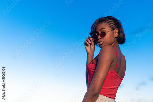 Black young woman posing confident holding a sunglasses during dusk © Iván Moreno