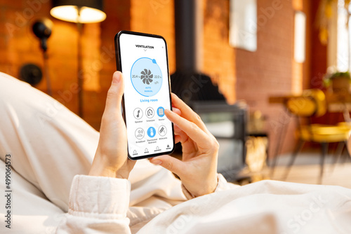 Woman holding phone with running smart home application for air conditioning on living room background. Close-up on device screen