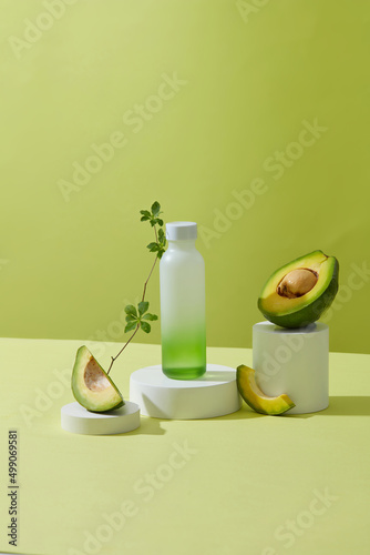 Fototapeta Naklejka Na Ścianę i Meble -  A front view of avocado and cosmetic jar decorated in white podium and green background 