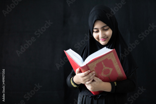 Valokuvatapetti muslim girl reading a holy book quran on black background