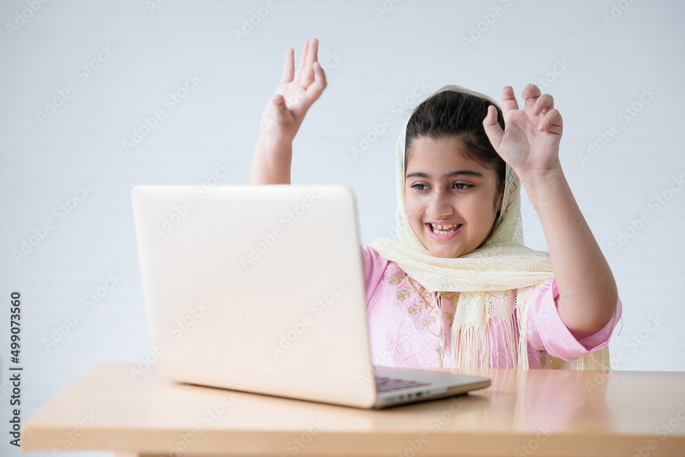 muslim girl using a laptop computer and raised hand for celebrating good news on the table muslim girl using a laptop computer and raised hand for celebrating good news on the table