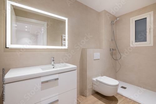 Modern bathroom with beige tiles  shower  toilet and rectangular large mirror with lighting
