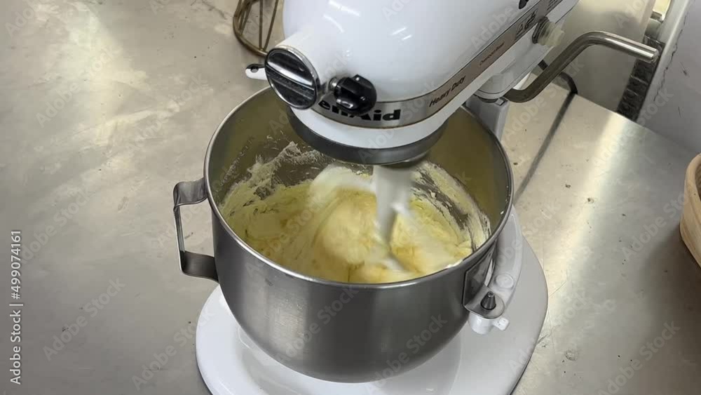 Tilt down shot of heavy duty kitchen appliance electric mixer with cake batter cake mixtures mixing smoothly and evenly in the stainless steel bowl.
