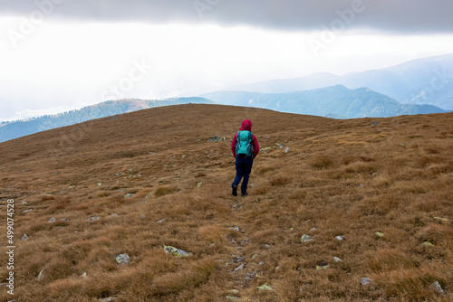 Woman hiking downhill from Haemmerkogel in the Lower Tauern mountain range, Styria, Austria, Europe. Autumn day in the Seckau Alps. Path on dry, bare terrain. Very cloudy, windy conditions
