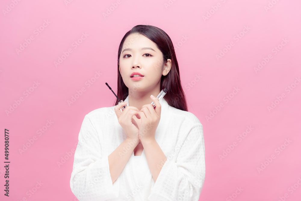 Dreaming asian woman with mascara for eyelashes with brush isolated over pink background Dreaming asian woman with mascara for eyelashes with brush isolated over pink background