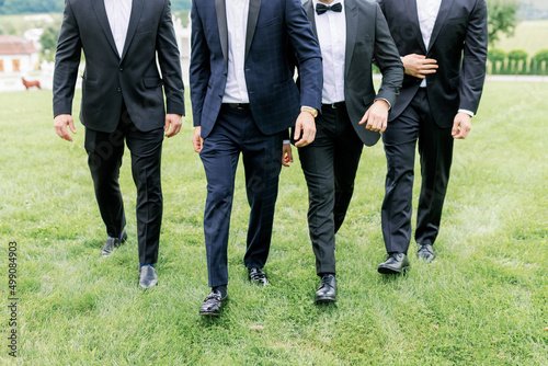 The groom and his friends walk on the green lawn, dressed in beautiful stylish suits. Large mans group of business executives approaching walking towards the camera led by a man