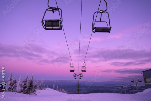 Ski lift in snowfall in mountains ski resort. Pink purple winter sunset view, landscape with chairlifts  and mountain skyline photo