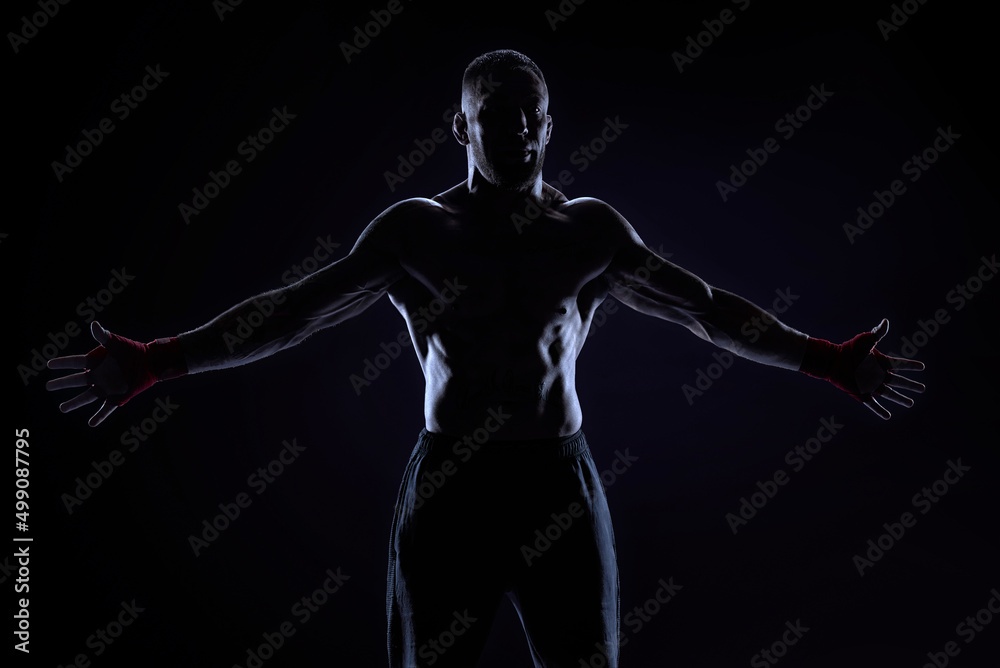 Kickboxer in red bandages poses on a blue background with his arms apart. The concept of mixed martial arts