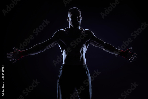 Fototapeta Naklejka Na Ścianę i Meble -  Kickboxer in red bandages poses on a blue background with his arms apart. The concept of mixed martial arts