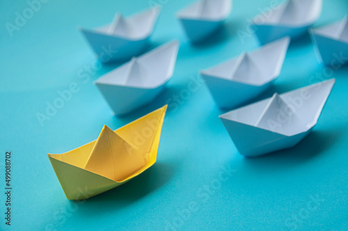 Leadership Concept - Yellow color paper ship origami leading the rest of the white paper ship on blue cover background. Copy space concept