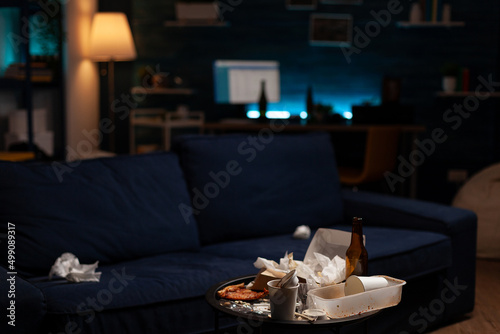 Empty unorganized space with dirty trash and stinky rubbish, messy unfinished food in leftovers cand and beer bottles on untidy table. Nobody in living room with unhealthy garbage.