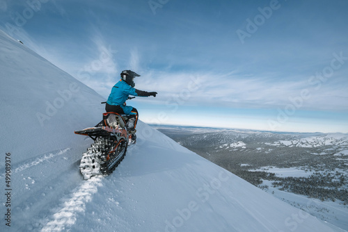 Snowbike rider on steep snowy slope. Modify motorcycle with ski and special snowmobile-style track instead of wheels photo
