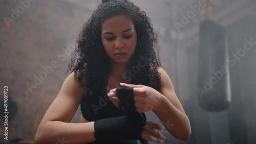 Young woman with dark kinky hair wraps hand for boxing