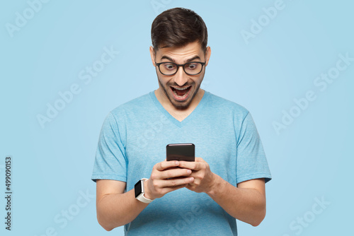 Young man holding phone in hands, looking at screen with excited wow face © Damir Khabirov
