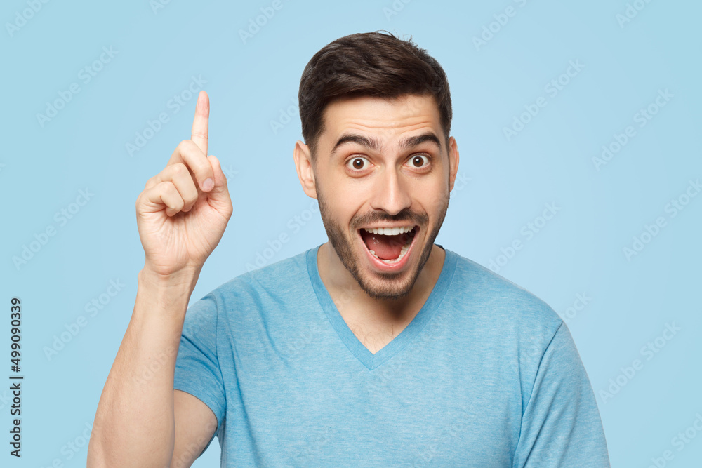 Young excited man in blue t-shirt, pointing upwards with finger, having great idea Young excited man in blue t-shirt, pointing upwards with finger, having great idea