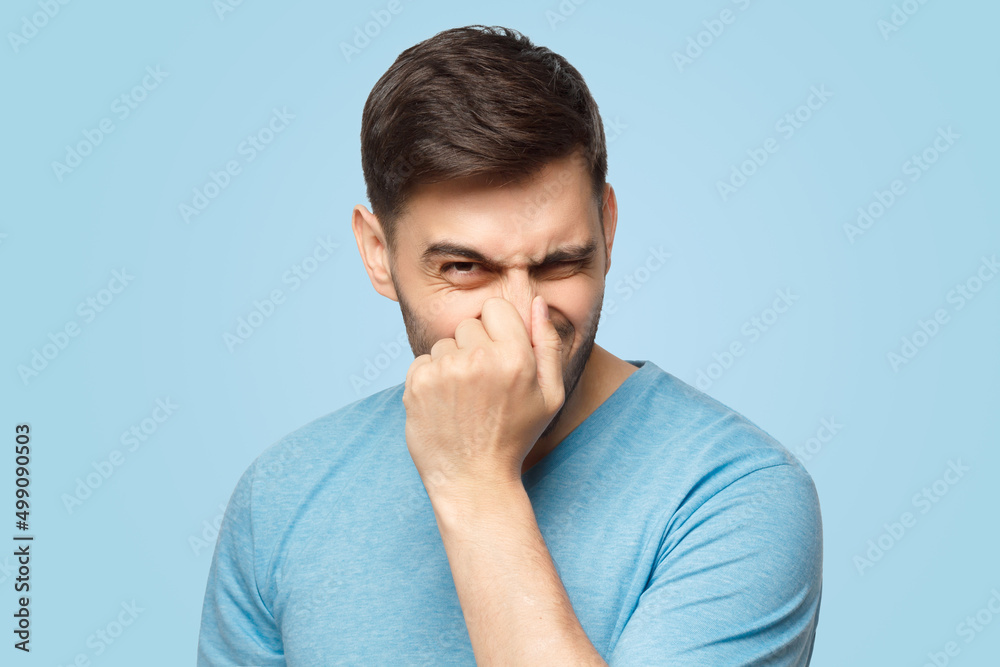 Young man holding his nose as if smelling something rotten and stinky